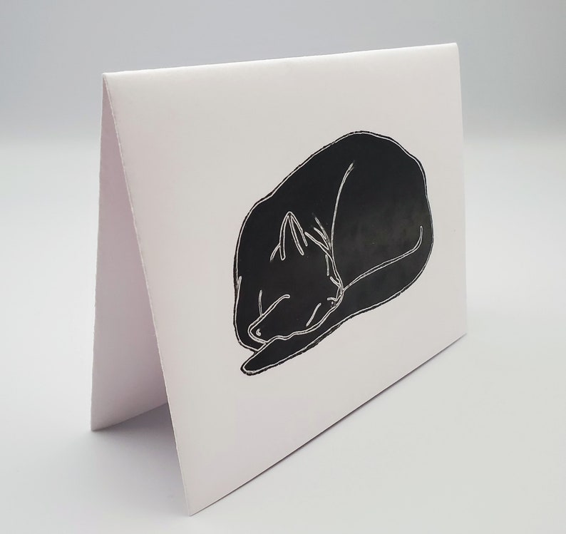May include: A black and white illustration of a cat curled up asleep on a white card.