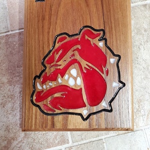 May include: Wooden bottle opener with a bulldog mascot design. The bulldog is red with white teeth and a black outline. The words "Devil Dogs" are engraved on the wood.