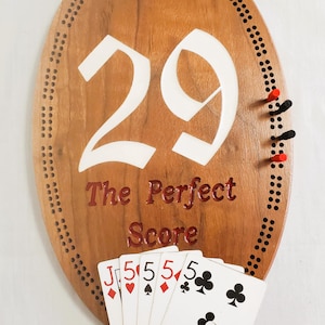 May include: Wooden cribbage board with the number 29 in white and the text "The Perfect Score" in red. Includes cribbage pegs and a hand of playing cards showing a Jack and four 5s.