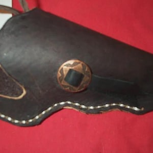 Può includere: Fondina in pelle nera con un bottone decorativo color rame. La fondina ha cuciture bianche lungo i bordi e un accento in pelle marrone. La fondina è progettata per contenere un'arma da fuoco.