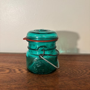 Tarro de cristal azul/verde con forma de bola, tapa y clip de cierre de alambre.