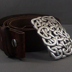 May include: A brown leather belt with a silver Celtic knot buckle. The buckle is a detailed design of interlocked knots.