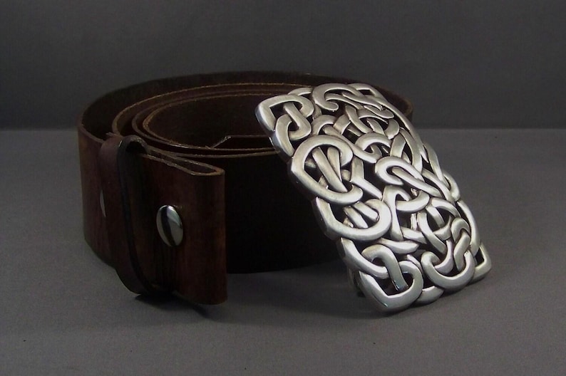 May include: A brown leather belt with a silver Celtic knot buckle. The buckle is a detailed design of interlocked knots.