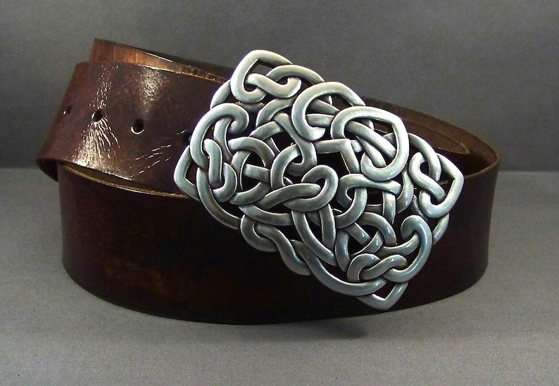 May include: A brown leather belt with a silver Celtic knot buckle. The buckle is intricate and detailed, with a woven design.