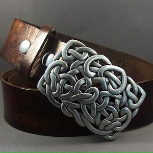 May include: A brown leather belt with a silver Celtic knot buckle. The buckle is intricate and detailed, with a woven pattern.