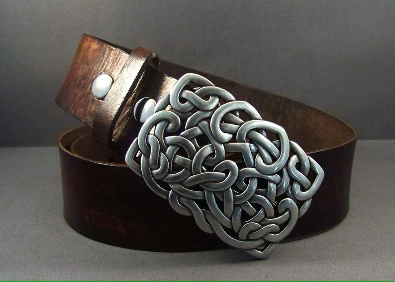 May include: A brown leather belt with a silver Celtic knot buckle. The buckle is intricate and detailed, with a woven pattern.