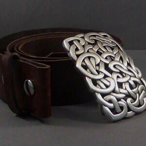 May include: A brown leather belt with a silver Celtic knot buckle. The buckle is a detailed design of interlocked loops.