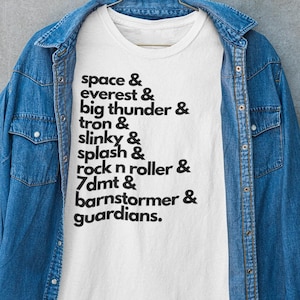 May include: White t-shirt with black text that reads "space & everest & big thunder & tron & slinky & splash & rock n roller & 7dmt & barnstormer & guardians."