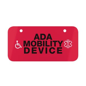 May include: Red rectangular sign with white text that reads "ADA MOBILITY DEVICE" with a wheelchair symbol on the left and a white star of life symbol on the right.