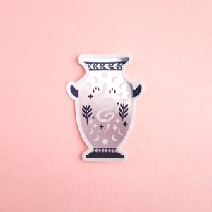 May include: A white ceramic vase with a black and silver design. The vase features a snake, stars, moons, and other celestial symbols.