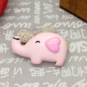 Pode incluir: Um pingente de elefante rosa com uma orelha em forma de coração e uma argola prateada. O elefante sorridente é decorado com glitter. Ideal para fazer joias.