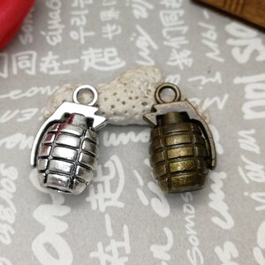 Op de afbeelding: Twee granaat-charms, een in zilver en een in brons. De zilveren charm heeft een getextureerd oppervlak en de bronzen charm heeft een glad oppervlak.
