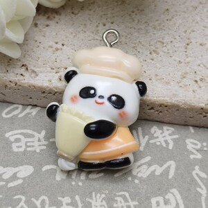 May include: A white and black panda bear charm with a yellow and orange chef's hat. The charm has a silver loop for attaching to a necklace or bracelet.