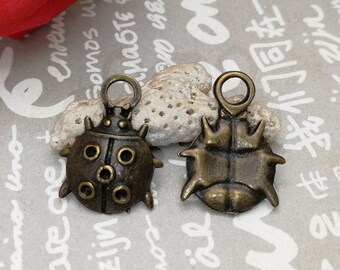May include: Two antique bronze charms in the shape of ladybugs. One ladybug charm has a more detailed design with a textured shell and a raised head. The other ladybug charm has a simpler design with a smooth shell and a flat head.