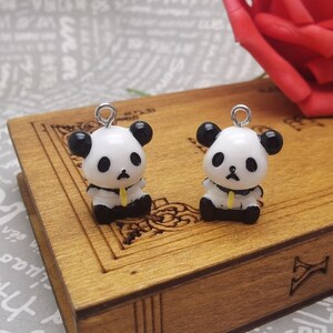May include: Two small black and white panda bear charms with yellow accents. The charms are hanging from silver jump rings.