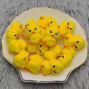 May include: A white plate with a gold rim holds a collection of yellow chick figurines. The chicks have black eyes and orange beaks.