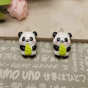 May include: Two panda bear charms. Each charm features a white body, black ears and arms, and a green bamboo shoot. The pandas have smiling faces with pink cheeks. Each charm has a silver loop at the top for attaching to jewelry.
