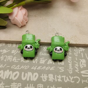 May include: Two green panda charms with silver jump rings. Each charm features a panda face with black eyes and a bamboo stalk with green leaves.