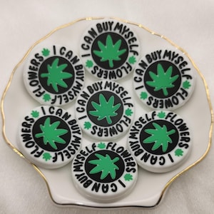 May include: Eight white round stickers with black and green designs. Each sticker has a green marijuana leaf and the text "I can buy myself flowers".