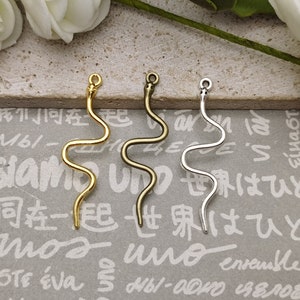 May include: Three wavy metal charms in gold, bronze, and silver. Each charm has a loop at the top for attaching to jewelry or other crafts.