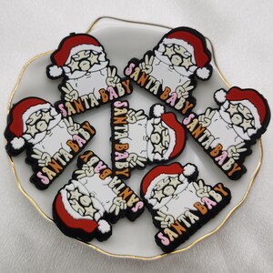 May include: Seven colorful Santa Claus charms with the text "Santa Baby" in pink, orange, and brown letters. The charms are made of silicone and have a glossy finish.
