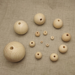以下が含まれることがあります： 中心に穴が開いた様々なサイズのウッドビーズのセット。ビーズはベージュの布地に円形に配置されています。