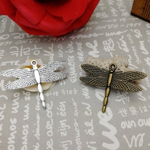 May include: Two silver and bronze dragonfly charms with intricate details. The charms are on a white background with Japanese and Korean text.