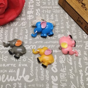 May include: Four colourful elephant charms with a loop for hanging. The elephants are made of plastic and are painted in shades of blue, pink, grey, and yellow. Each elephant has a different colour for its ears and trunk.