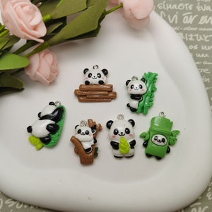 May include: Seven panda charms with different designs. The charms are made of white and black polymer clay and feature pandas holding bamboo, sitting on a log, and climbing a tree. The charms are perfect for adding a touch of whimsy to jewelry, keychains, or other crafts.