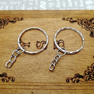 May include: Two silver keychains with a chain attached to each ring. The keychains are on a wooden surface.