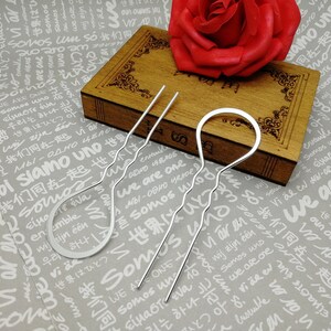 Puede incluir: Tres pinzas para el pelo plateadas con dise&ntilde;os ondulados. Las pinzas est&aacute;n sobre una superficie de madera con una rosa roja en el fondo.