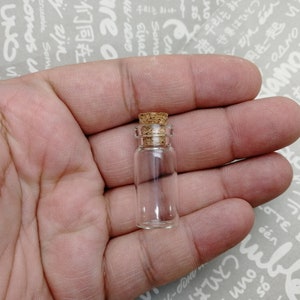 May include: A small, clear glass bottle with a cork stopper. The bottle is held in a hand.
