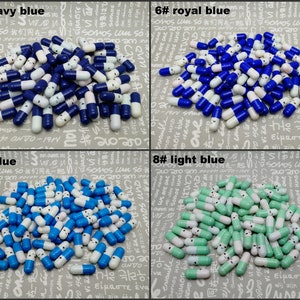 以下が含まれることがあります： 白と青のカラーリングの小さなプラスチックカプセルが詰め合わせになっています。カプセルは4つのグループに分けられており、それぞれ異なる青色の濃淡になっています。濃紺、ロイヤルブルー、青、水色です。各グループには番号と色の名前が付けられています。