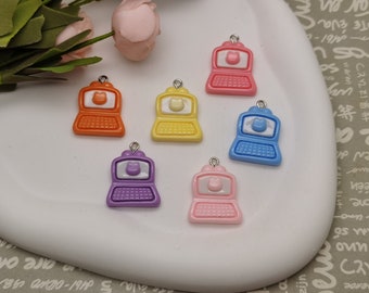 May include: Six colourful laptop charms with a white cat face on the screen. The charms are made of plastic and have a silver loop for attaching to a keychain or bag.
