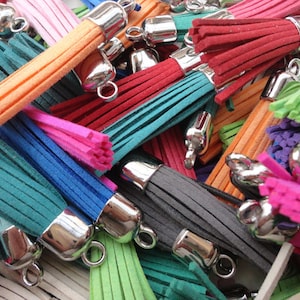 May include: Assortment of colorful suede tassels with silver metal rings. The tassels are in various colors, including pink, red, orange, green, blue, and gray.
