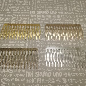 Pode incluir: Dois pentes de cabelo, um dourado e outro prateado, com um design decorativo. Os pentes estão sobre um fundo com as palavras "noi siamo uno" e "we are one" escritas em vários idiomas.