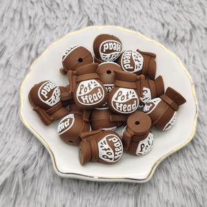 May include: A pile of brown silicone beads with white lettering that reads "Pot Head".