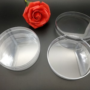 Op de afbeelding: Drie transparante ronde plastic containers die op elkaar gestapeld zijn. De containers zijn leeg en hebben een glad, glanzend oppervlak.