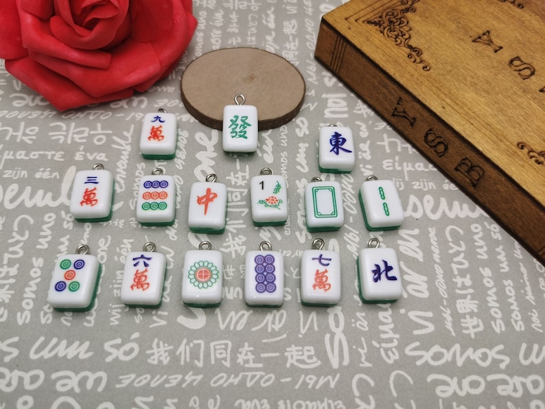 May include: A collection of 14 colorful Chinese Mahjong tile charms with green, red, white, and blue accents. The tiles feature various Chinese characters and symbols.