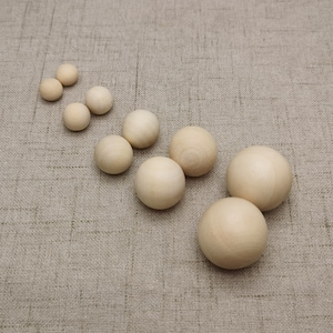 May include: A set of ten wooden balls of varying sizes, arranged in a diagonal line on a beige fabric surface.