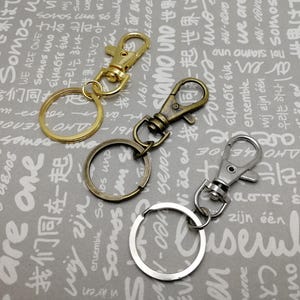 May include: Three keychains with different colored metal rings and clasps. The keychains are on a gray background with white text.