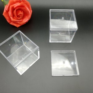 May include: Three clear plastic square boxes with lids. The boxes are empty and are sitting on a black surface.