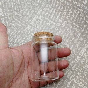 May include: A clear glass bottle with a cork stopper. The bottle is empty and has a round shape.