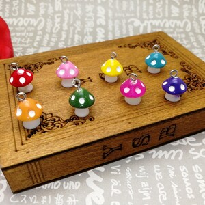 May include: A collection of ten colourful mushroom charms with white polka dots. The charms are arranged on a wooden surface with a decorative design.