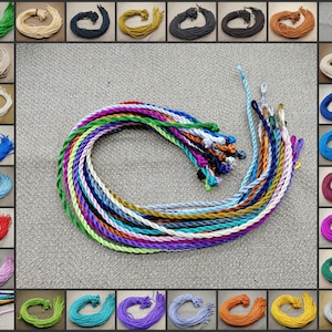 May include: A collection of 24 spools of colourful waxed cord, each wound with a different colour of thread. The cords are arranged in a grid pattern, with each spool in its own square. The cords are all the same size and thickness, and they are all made of the same type of waxed thread.