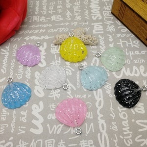 Pode incluir: Conjunto de dez pingentes de concha marinha coloridos com argolas de salto prateadas. As conchas marinhas são feitas de resina e têm um acabamento brilhante. As cores incluem rosa, azul, branco, preto, amarelo e verde.