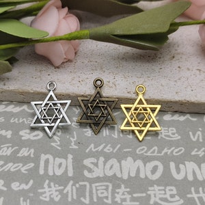 May include: Three silver-toned Star of David charms with a double-layered design. The charms are on a white surface with printed text.