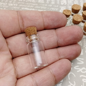 May include: A small, clear glass bottle with a cork stopper. The bottle is held in a hand.