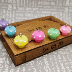 May include: Six colourful mushroom charms with white polka dots and silver loops. The charms are arranged on a wooden book with Japanese text.
