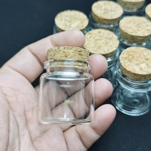 May include: A group of small glass bottles with cork tops. The bottles are clear and the corks are brown. The bottles are arranged in a row on a black surface.